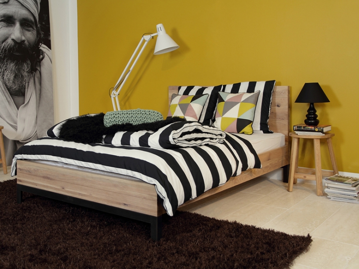 Dřevěná postel s černo-bílým povlečením a nočním stolkem s lampou
